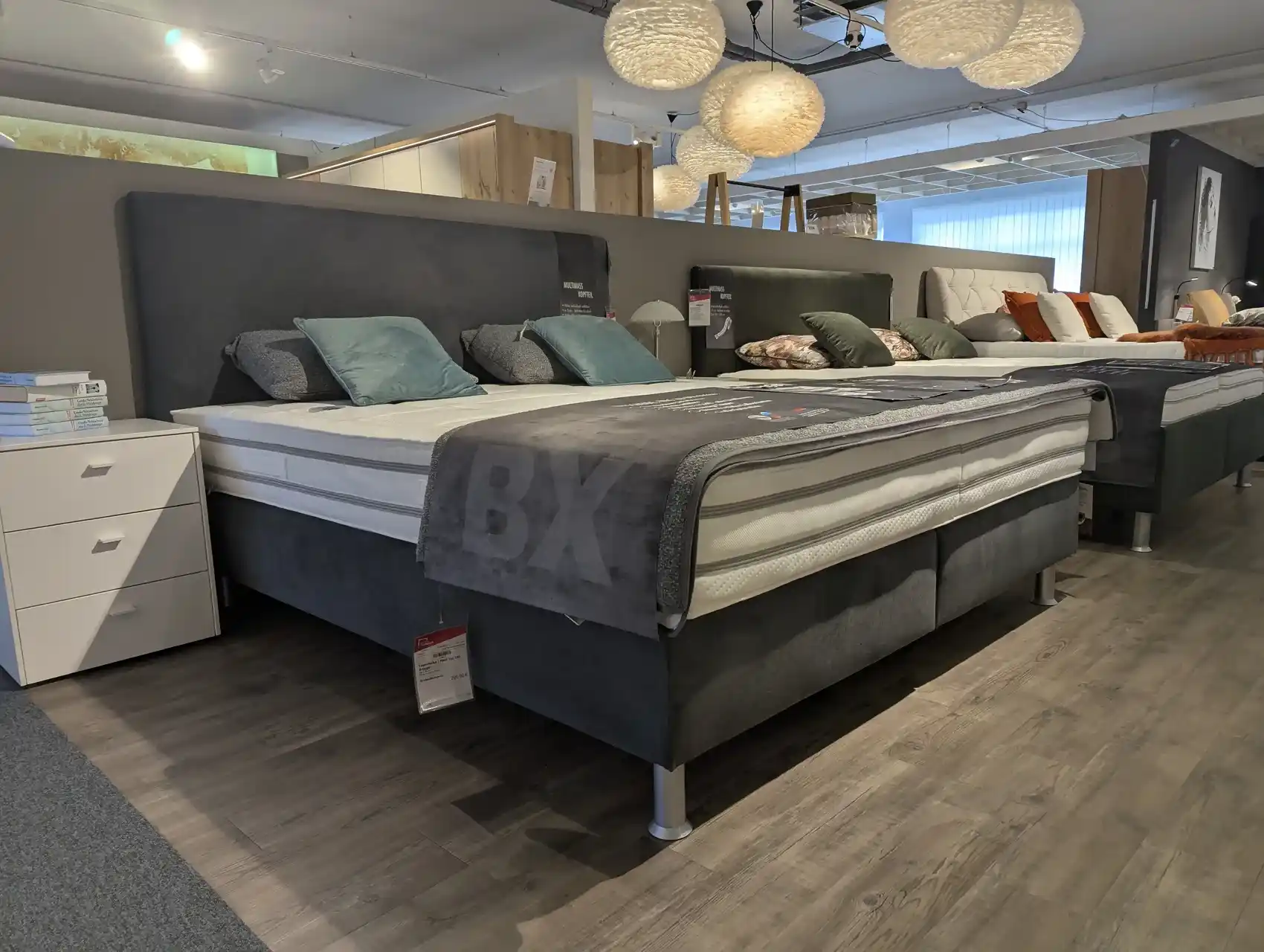 Boxspringbett mit Stoffbezug in Seitenansicht mit gepolstertem Kopfteil im Ausstellungsraum