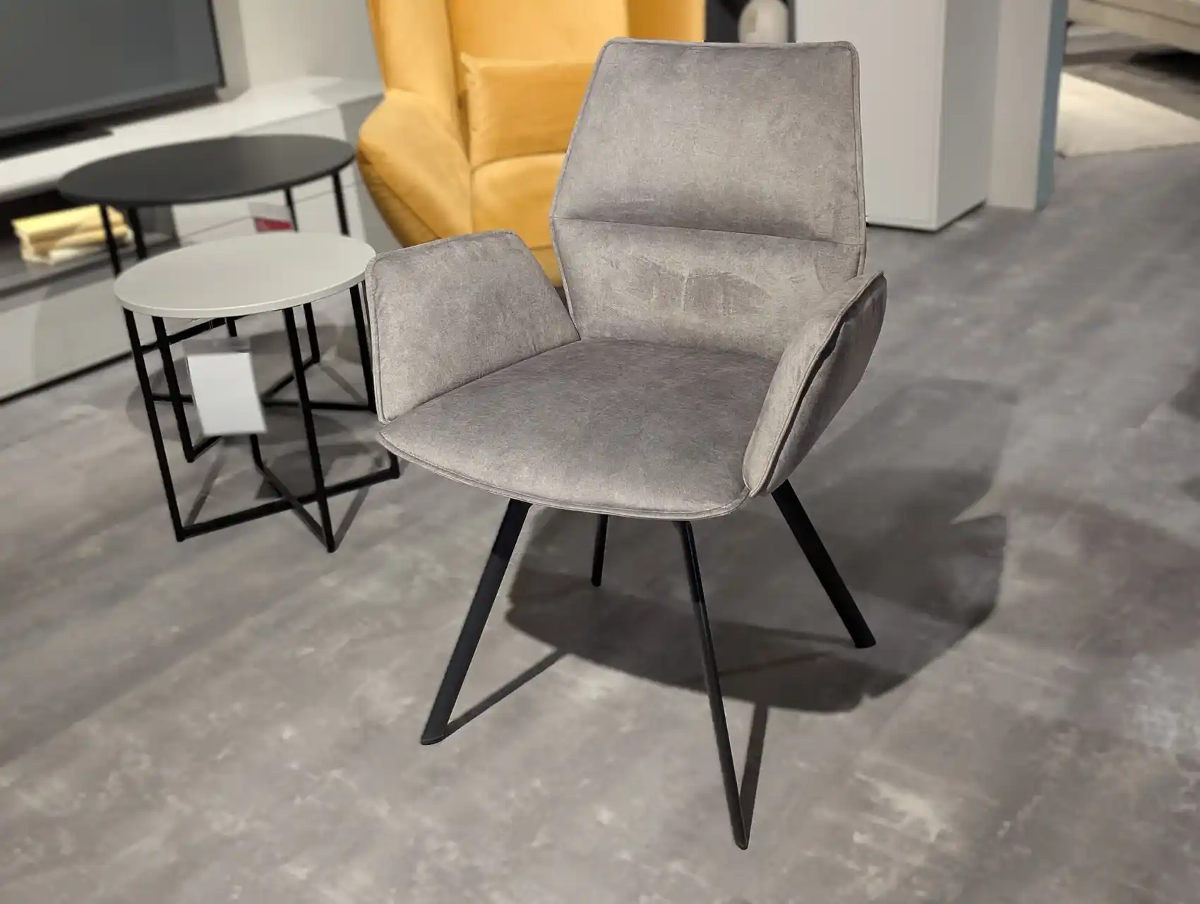 Grauer Stuhl mit Stoffbezug. Der Stuhl ist drehbar und hat Armlehnen.